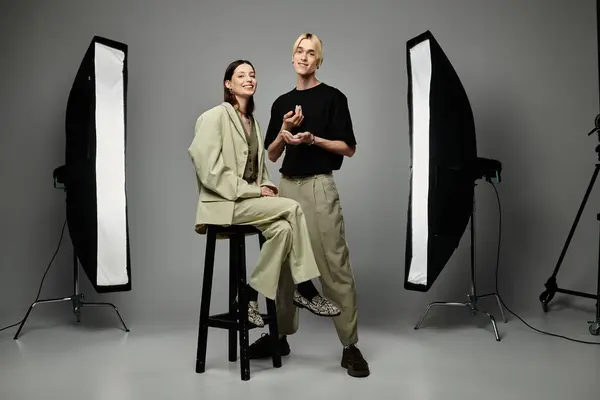 Artista de maquillaje masculino embellece cliente femenino en frente de equipo de fotos. - foto de stock