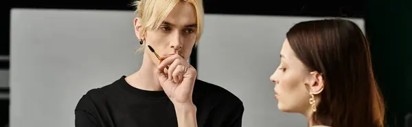 A woman sits next to a man in a black shirt, receiving makeup application. — Stock Photo