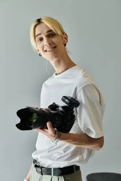 Cheerful man holds camera, smiles on gray backdrop. — Stock Photo