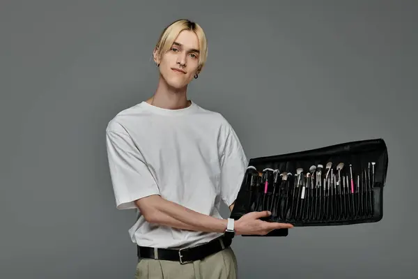 Handsome man in a fashionable outfit holding a compact case filled with makeup brushes. — Stock Photo