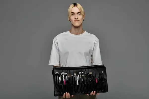 Stylish young man holding a black case full of makeup brushes. — Stock Photo