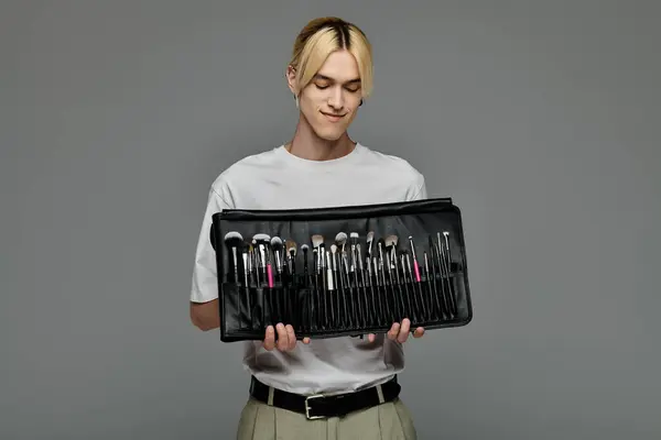 Ein stilvoller Mann hält anmutig eine vielfältige Sammlung von Make-up-Pinseln in der Hand. — Stockfoto