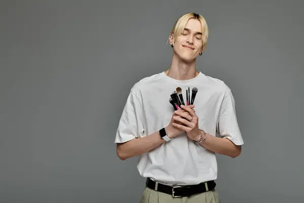 Young man skillfully holds a variety of makeup brushes. — Stock Photo