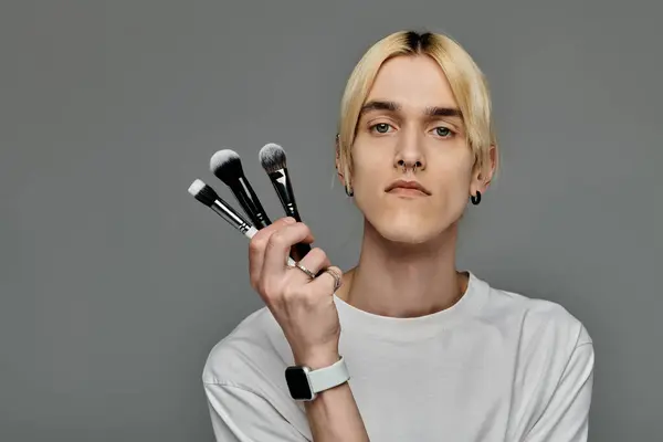 A man elegantly holding three makeup brushes in his hand. — Stock Photo