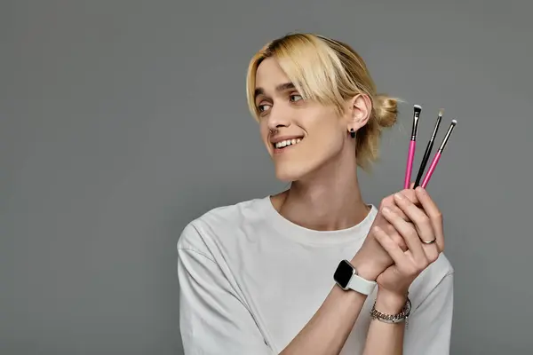 Handsome man in a fashionable outfit holding makeup brushes. — Stock Photo