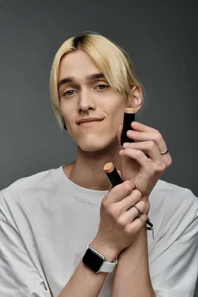 A stylish man confidently holds a makeup product in his hand. — Stock Photo