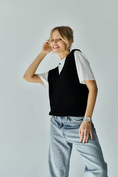 Стильная молодая женщина с светлыми волосами в черно-белом свитере и джинсах на сером фоне. — стоковое фото