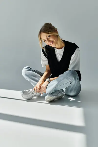 A young woman with blonde hair sits on the ground, legs crossed, exuding peace and grace in stylish attire. — Stock Photo