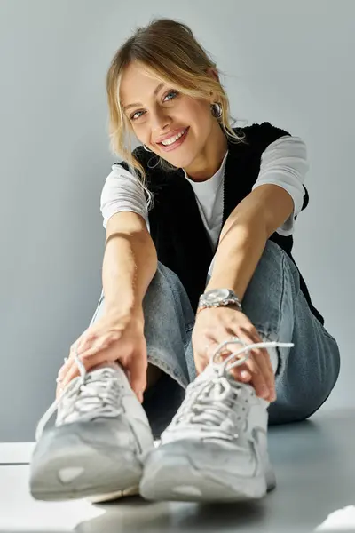 A young, beautiful woman with blonde hair tying her shoes while sitting on the floor in stylish casual attire. — Stock Photo
