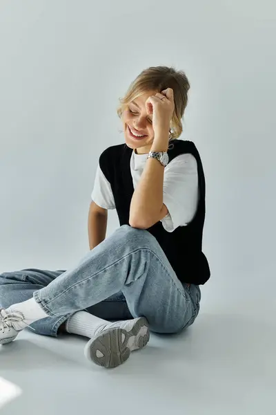A young woman with blonde hair and stylish attire sits on the floor with her hand on her head in a moment of reflection. — Stock Photo