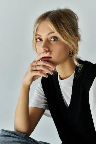 A young woman with blonde hair sits on the ground, deep in thought, with her hand resting on her chin. — Stock Photo