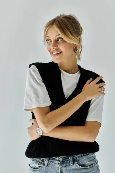 Stylish young woman with blonde hair poses confidently with crossed arms on a grey background. — Stock Photo