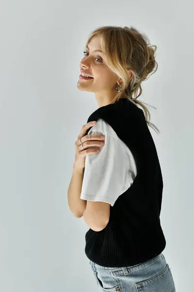 A young, beautiful woman in black and white shirt and jeans, posing confidently against a grey background. — Stock Photo