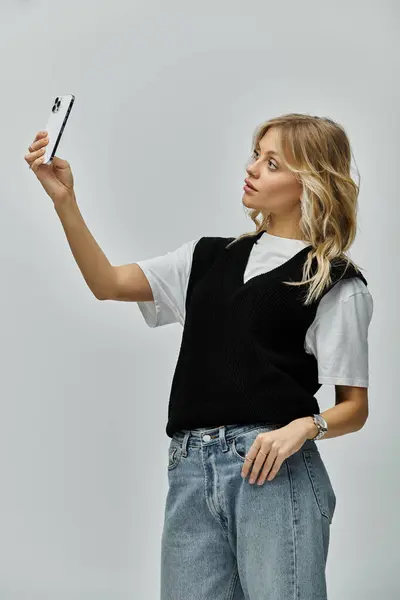 Una joven elegante con el pelo rubio sosteniendo un teléfono celular en su mano derecha sobre un fondo gris. — Stock Photo