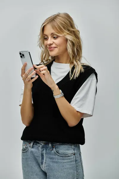 Stylish young blonde woman holding a cell phone in her hands against a grey background. — Stock Photo