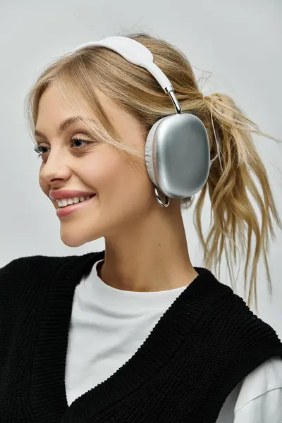 A stylish young woman with blonde hair listens to music on headphones against a grey backdrop. — Stock Photo
