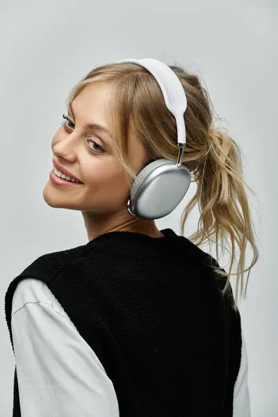 A young woman with blonde hair wearing headphones on a gray background. — Stock Photo