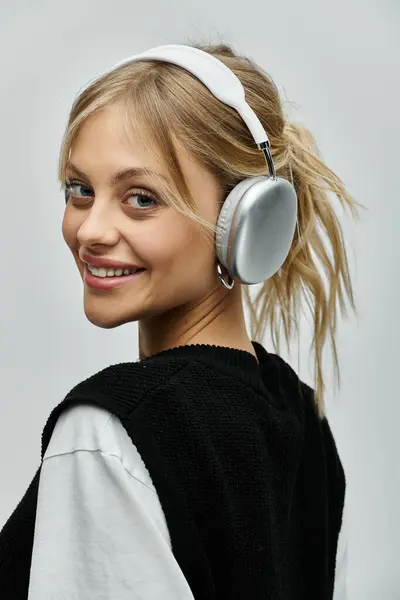 A young woman with blonde hair wearing headphones smiles warmly at the camera against a grey backdrop. — Stock Photo