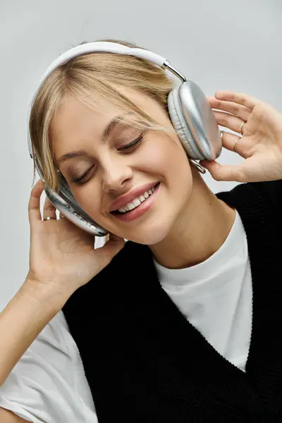 A young, beautiful woman with blonde hair wearing headphones, lost in the music, on a grey background. — Stock Photo