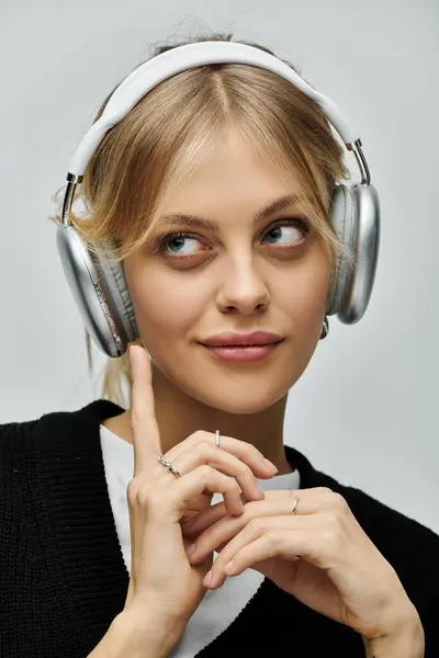 Eine junge Frau mit blonden Haaren trägt Kopfhörer und Pullover, sieht gemütlich und zufrieden aus. — Stockfoto