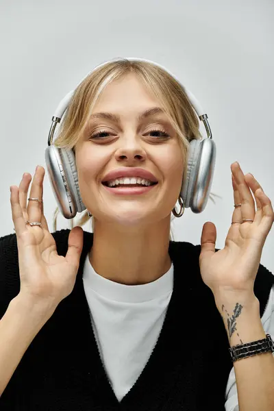 A young blonde woman in stylish casual attire smiles while listening to music through headphones. — Stock Photo