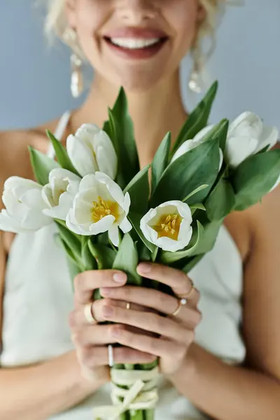 A blonde woman exudes elegance while holding a bouquet of delicate white flowers against a grey backdrop. — Stock Photo