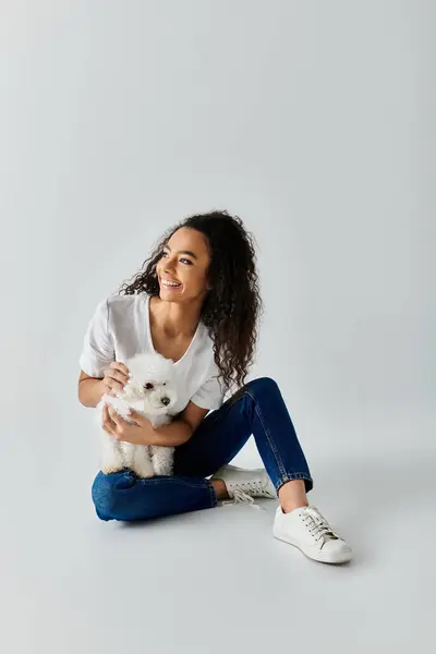 Женщина сидит на полу, нежно держа белого Бишона Фризского пса. — стоковое фото