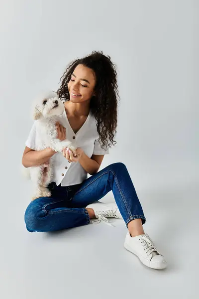 Una donna si siede pacificamente sul pavimento, teneramente tenendo il suo adorabile bichon frise dog. — Foto stock