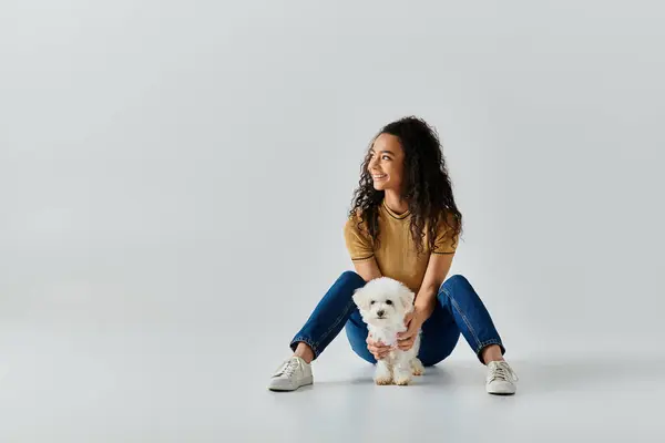 A woman sits peacefully on the floor beside her white bichon frise dog. — Stock Photo