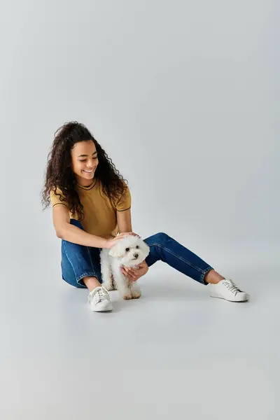 A young woman sitting on the floor, tenderly holding her white Bichon Frise dog. — Stock Photo