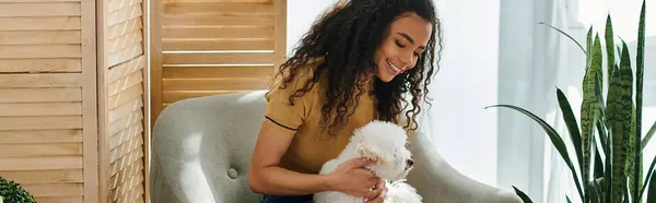 Una giovane donna seduta, culla tra le braccia di un bianco Bichon Frise. — Foto stock