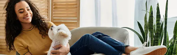 Woman in chair cuddling her fluffy Bichon Frise dog. — Stock Photo
