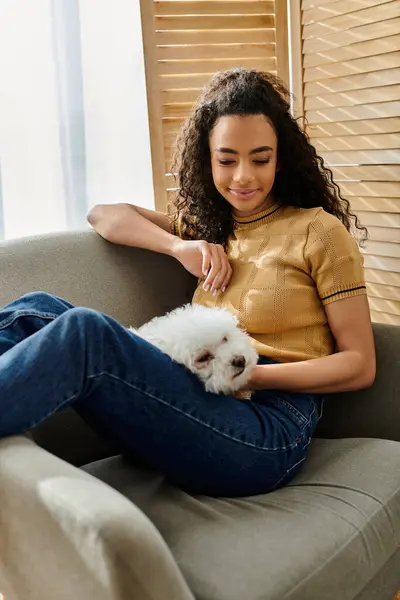 Una donna si rilassa sul divano mentre tiene il suo piccolo cane bianco. — Foto stock