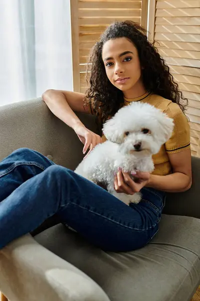 Woman sits on couch, holding white bichon frise dog. — Stock Photo