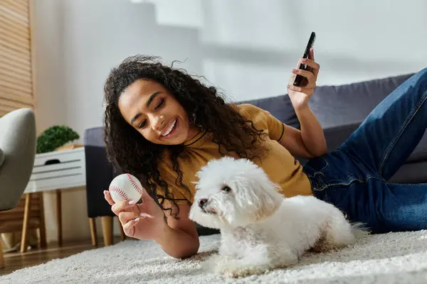 A woman lounging with her bichon frise and checking her phone. — Stock Photo