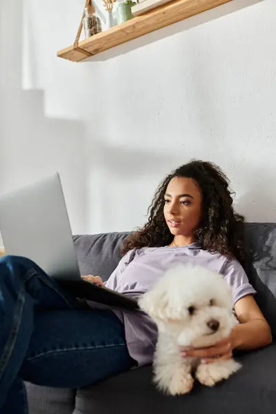 Woman on couch with laptop and bichon frise dog. — Stock Photo