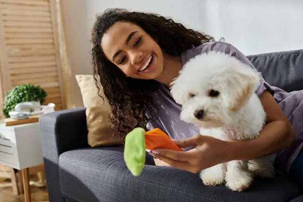 A young woman peacefully sitting on a couch, holding her fluffy white Bichon Frise dog. — Stock Photo