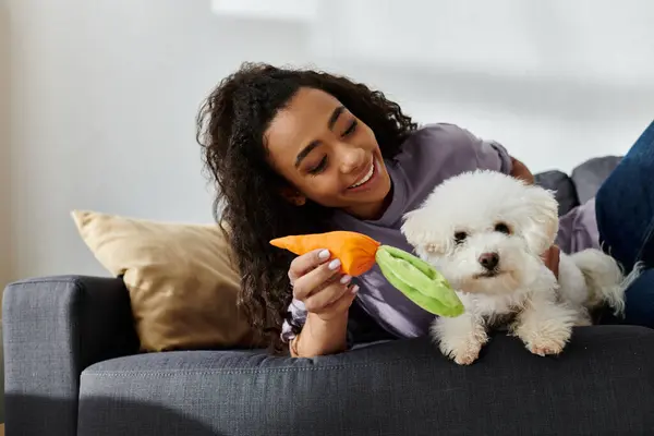 A young woman lounges with her adorable bichon frise dog and a toy. — Stock Photo
