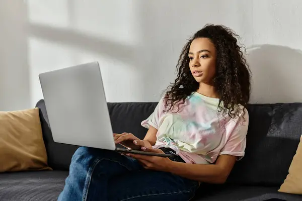 A woman sits on a couch, multitasking with her laptop. — Stock Photo