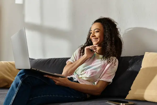 Woman seated on cozy couch, absorbed in laptop screen. — Stock Photo