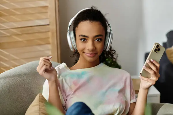 Woman on couch, wearing headphones, with cellphone. — Stock Photo