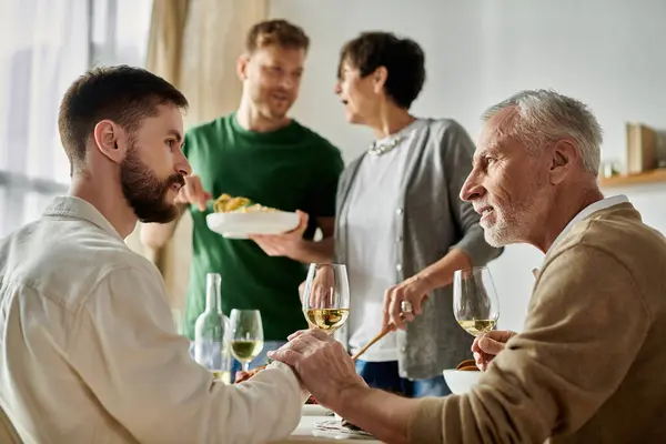 A gay couple sits at a table with parents, enjoying a meal and conversation. — Stock Photo