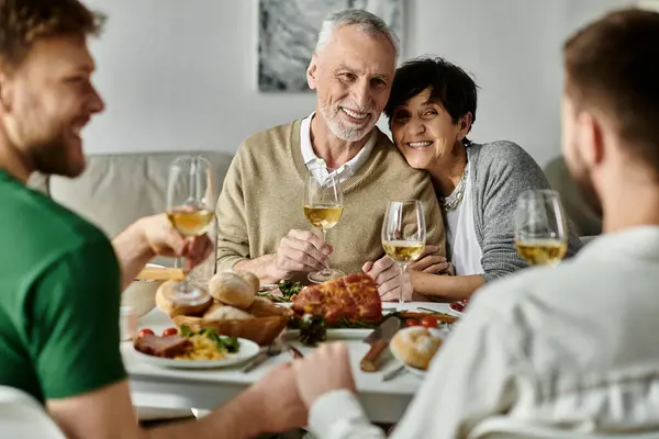 A gay couple shares a celebratory dinner with their families, with smiles and wine glasses raised in a toast. — Stock Photo