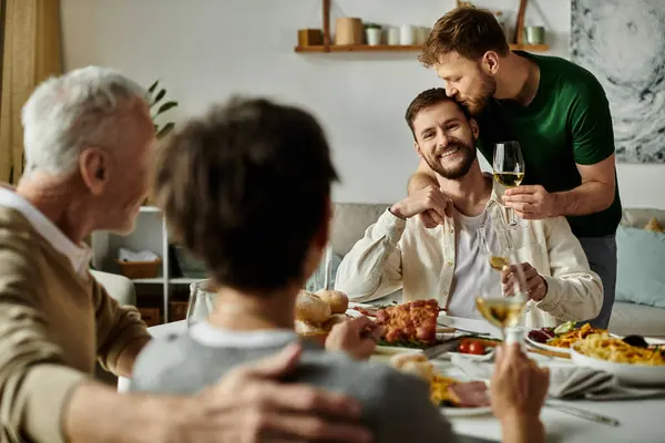 A gay couple enjoys dinner with parents, with one partner receiving a loving kiss on the head. — стоковое фото
