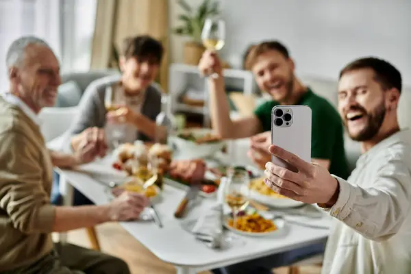 Una pareja gay se toma una selfie con su familia durante una comida. - foto de stock