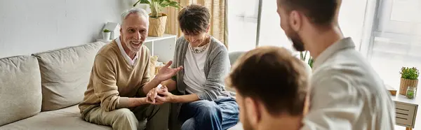 A gay couple sits with parents on a couch in their home, having a conversation. — Stock Photo