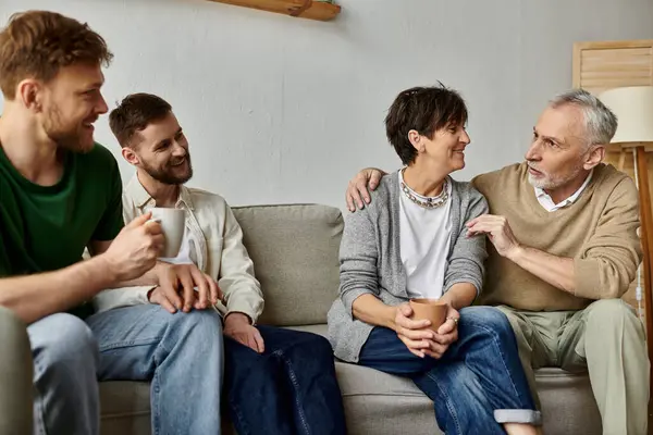 A gay couple sits with parents on a couch, engaging in a warm and intimate conversation. — стоковое фото