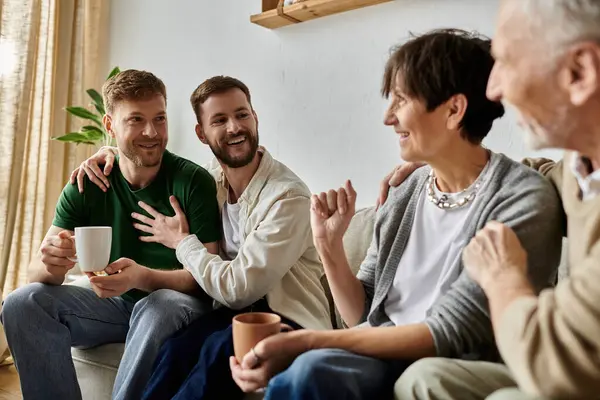 A gay couple sits on a couch with parents, all smiling and laughing together. — Stock Photo