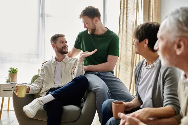 Una coppia gay si siede con i genitori in un soggiorno, avendo una conversazione. — Foto stock
