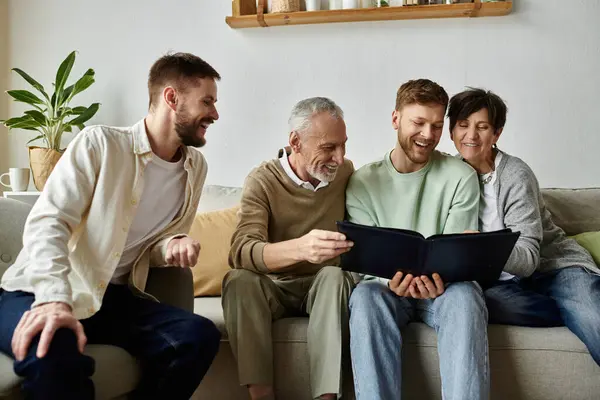 A gay couple laughs with parents while looking at an old photo album together on the couch. — Stock Photo